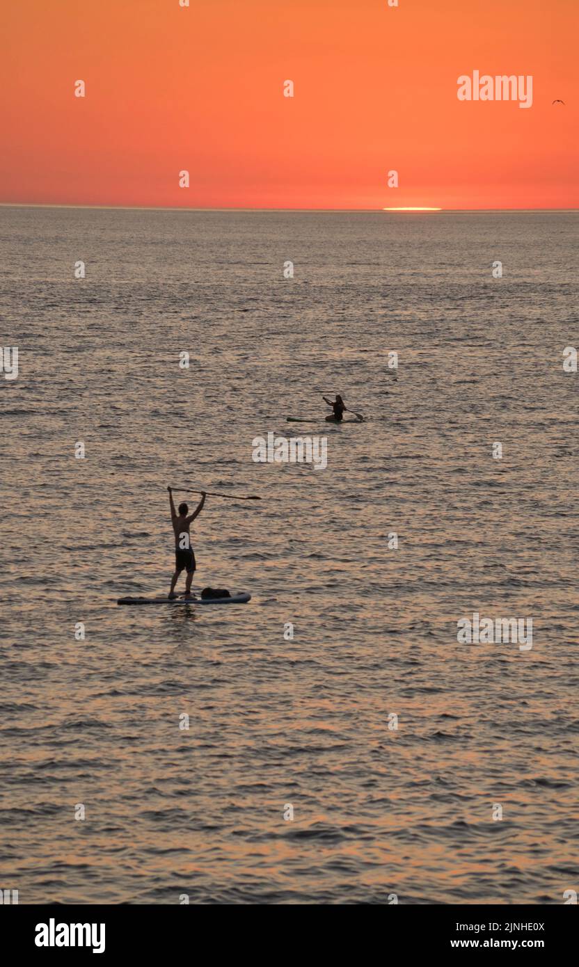 Holidaymakers paddle boarding at sunset and swimming in the sea under heatwave on beach in Aberystwyth,Ceredigion,Wales,UK Stock Photo