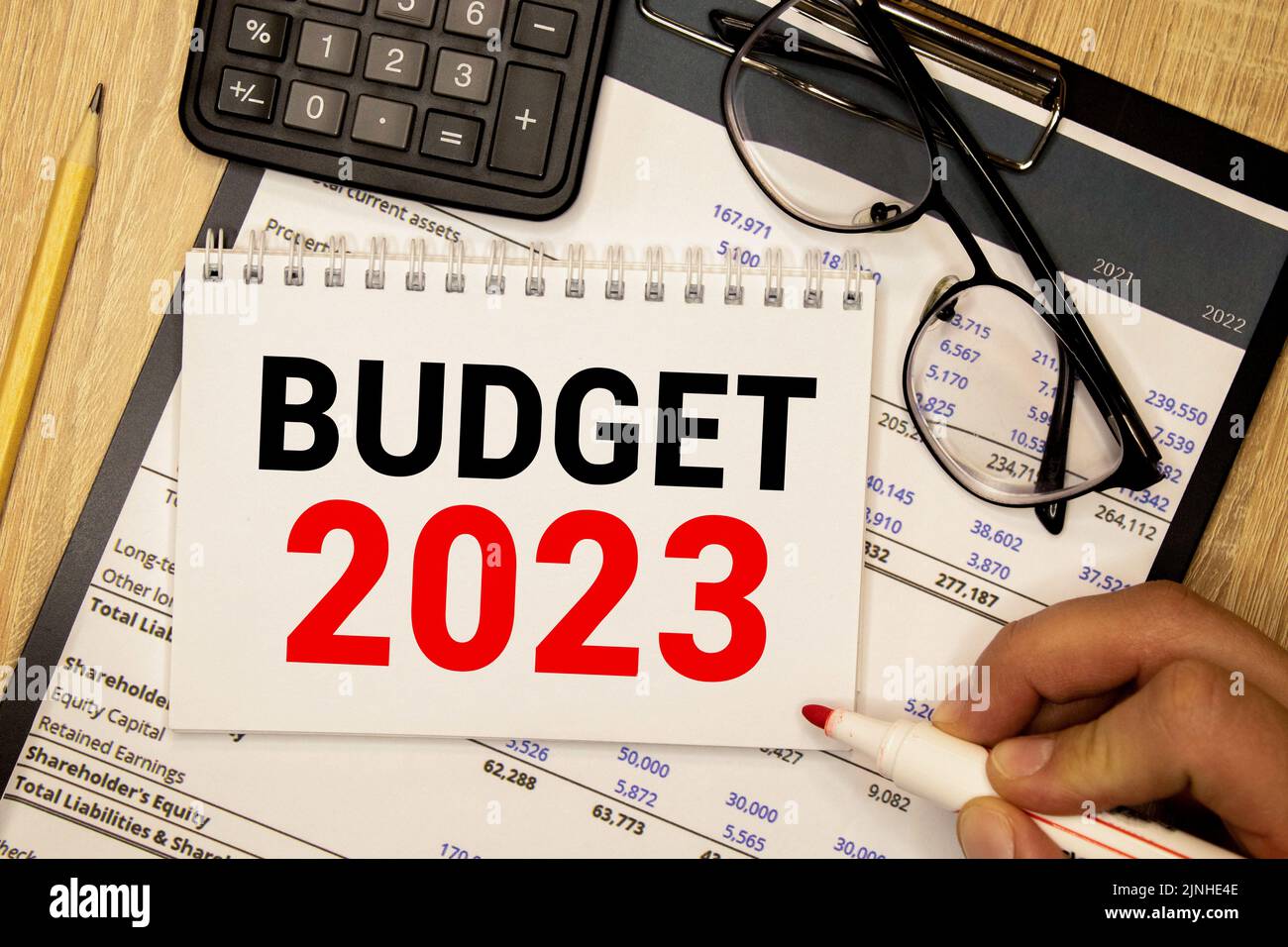 Folded business papers, pen, glasses, a flower in a pot and a tablet with a sheet of paper with the text BUDGET 2023 on the desktop. Top view of the w Stock Photo