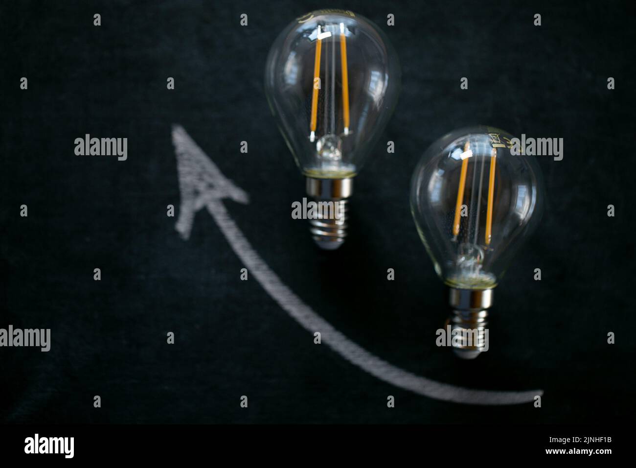 Rising electricity prices.Light bulb and up arrowon on a black chalk board.Electricity cost.Crisis of energy production.Increasing the cost of light Stock Photo
