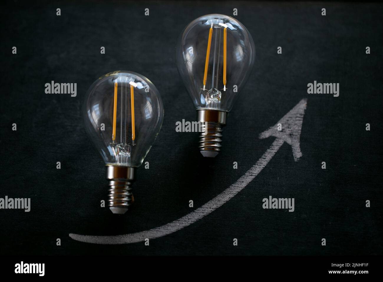 Light bulb and up arrowon on a black chalk board.Electricity cost.Crisis of energy production.Increasing the cost of light and heat.Saving electricity Stock Photo