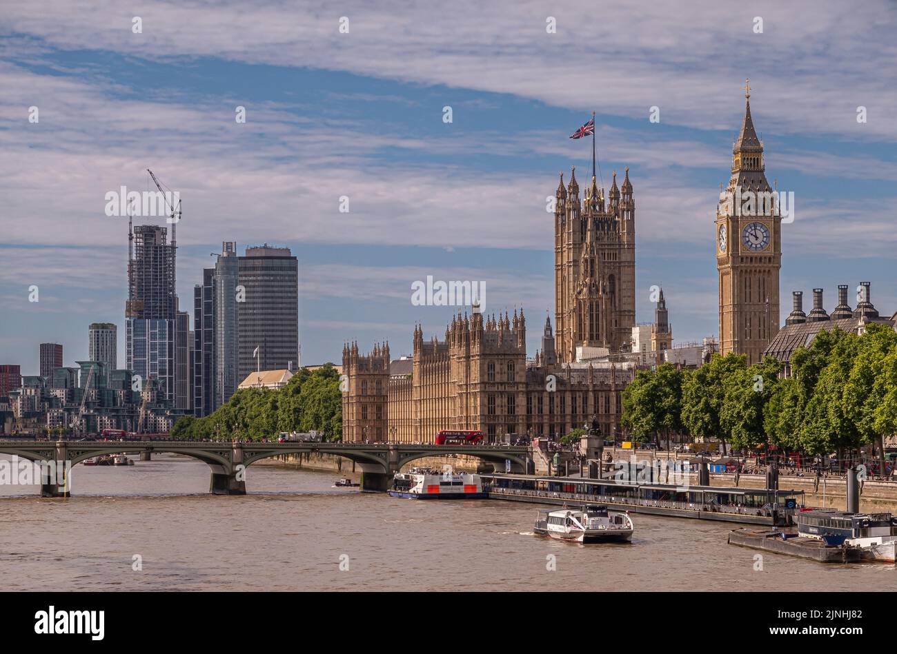 London, UK - July 4, 2022: Wide scenery with Palace of Westminster, House of Lords, Big Ben, church towers, and further city highrises under blue cllu Stock Photo