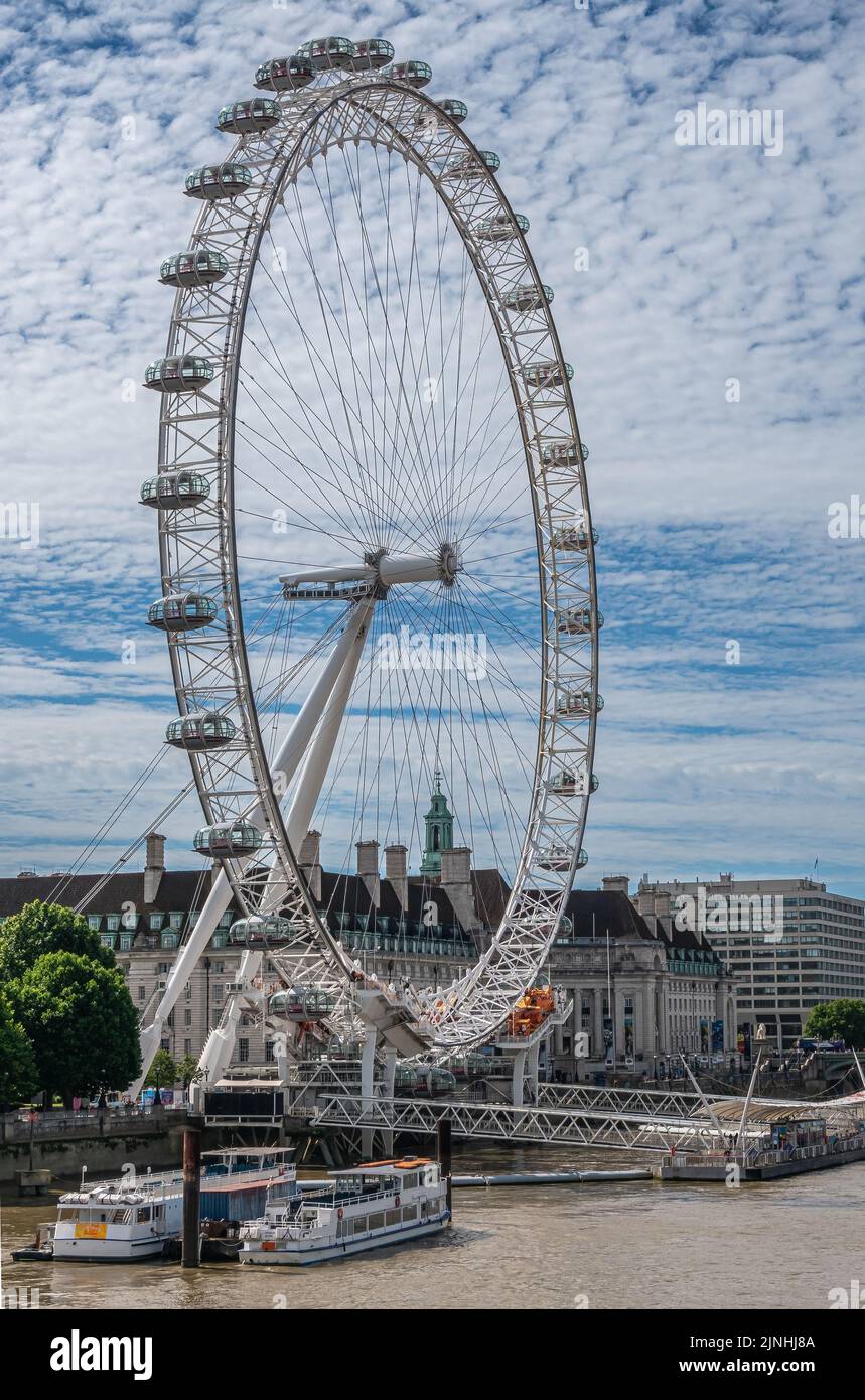 London, UK - July 4, 2022: Closeup of White London Eye against blue cloudscape. Brown water Thames River in front. Cityscape of multi-story buildings Stock Photo