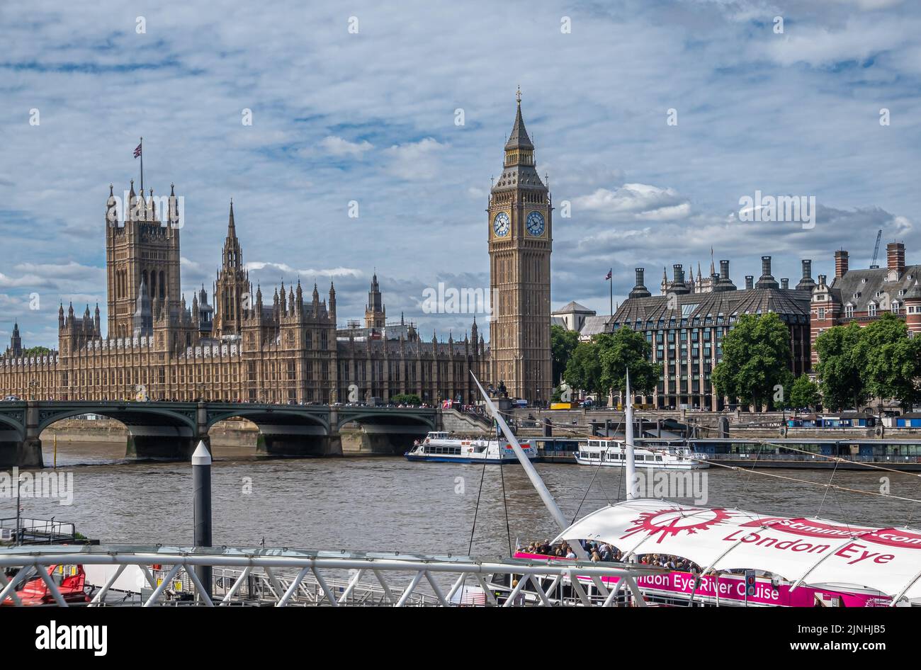 London, UK - July 4, 2022: London Eye cruise boat on Thames river with Westminster Palace, bridge and Big Ben in back under blue cloudscape. Other bui Stock Photo