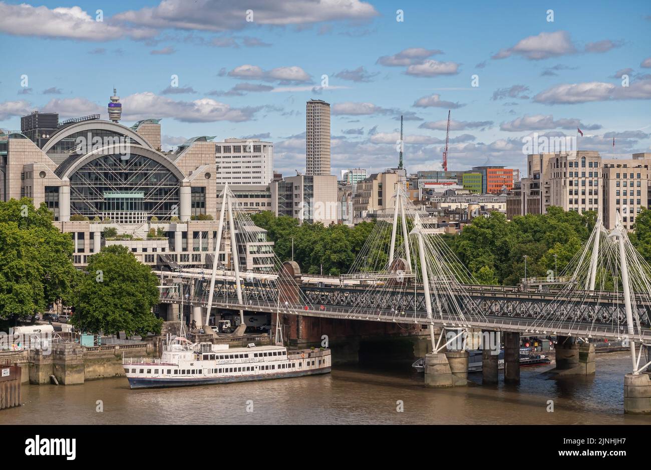 London, UK - July 4, 2022: Cityscape focus on Sharing Cross railway station with Hungerford and Golden Jubilee bridges crosseing brown water Thames Ri Stock Photo