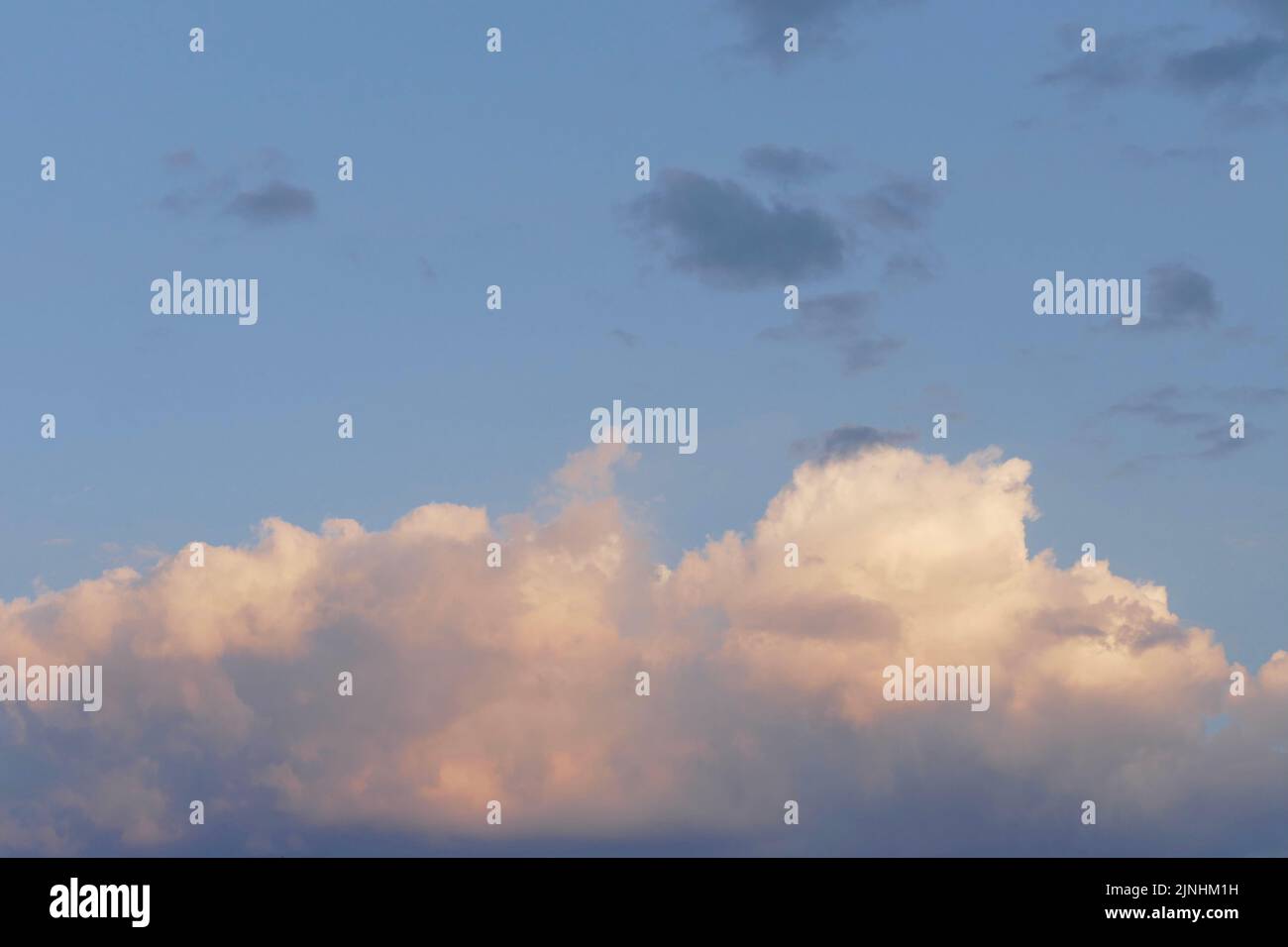 soft blue sky with fluffy white clouds tinged with pink and peach Stock Photo