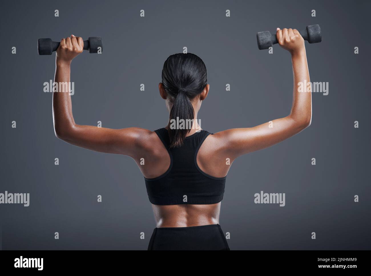 Tone those arms. Studio shot of a sporty young woman lifting weights