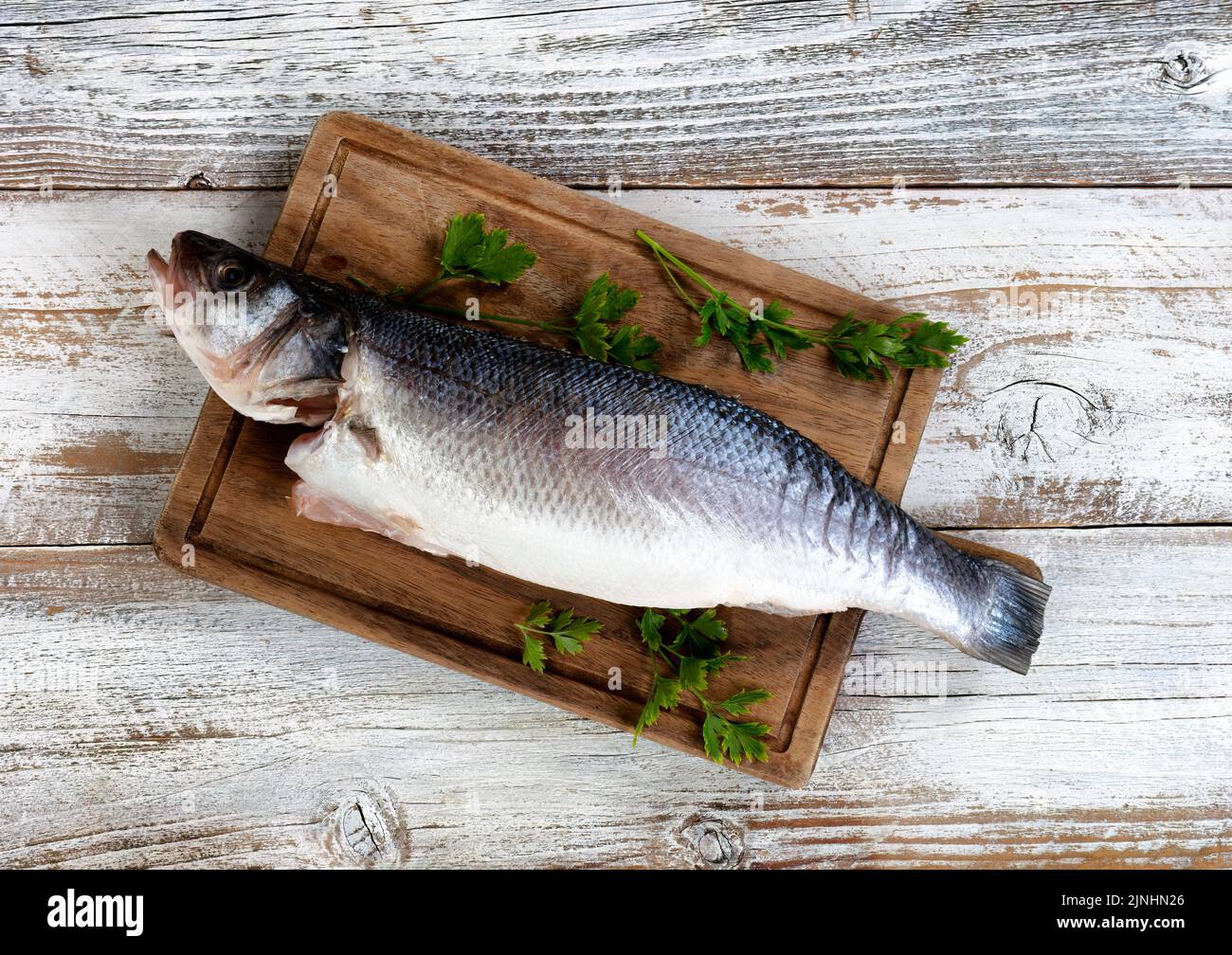 Freshly cleaned seafood seabass fish on wood board with parsley herbs on side Stock Photo
