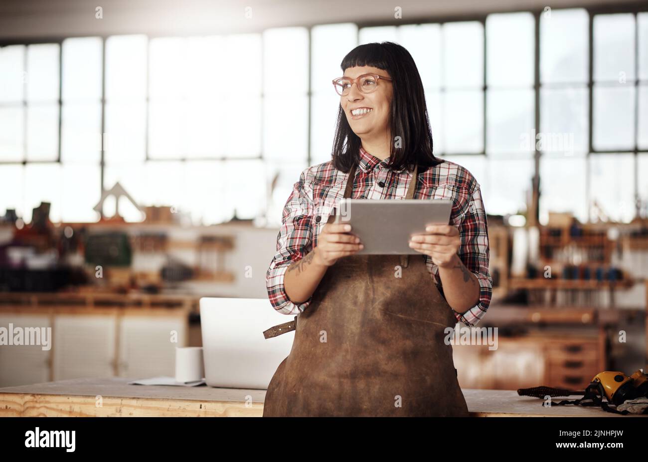 This will work... an attractive young woman looking thoughtful while working on her tablet in her creative workshop. Stock Photo