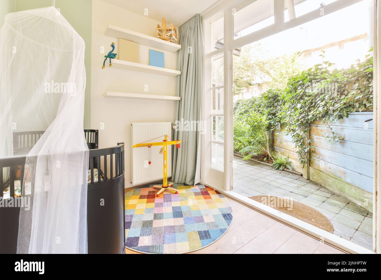 Interior of white room with baby crib near window with blue chest of