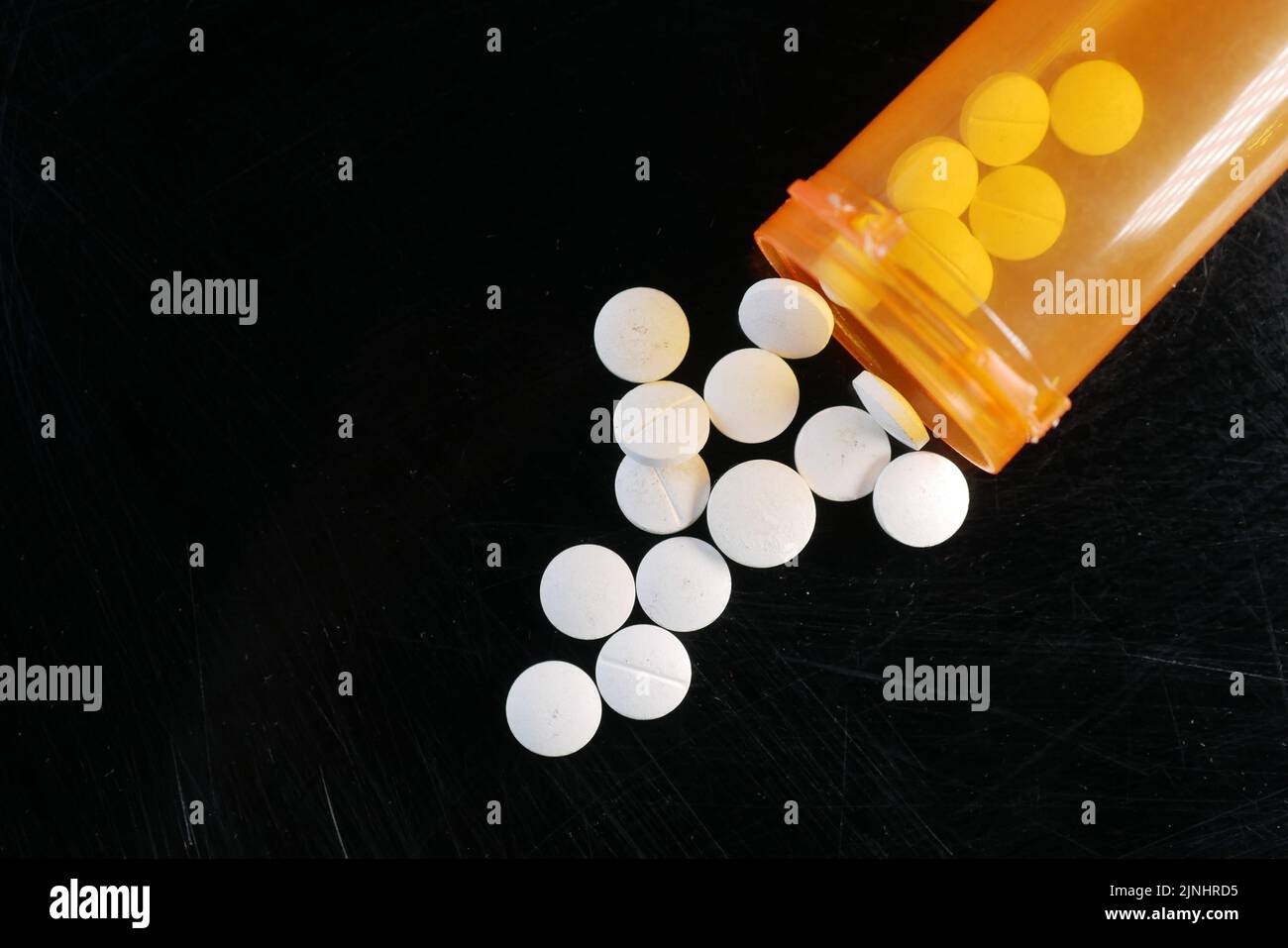 white color medical pills spilling from a orange color container on black  Stock Photo