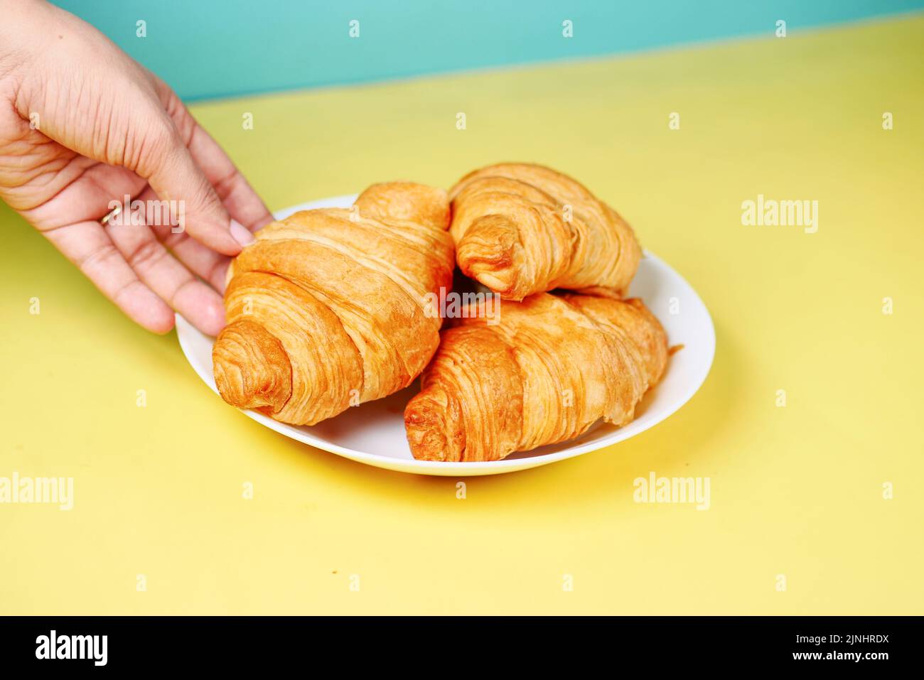 hand pick a fresh baked croissant from a plate  Stock Photo