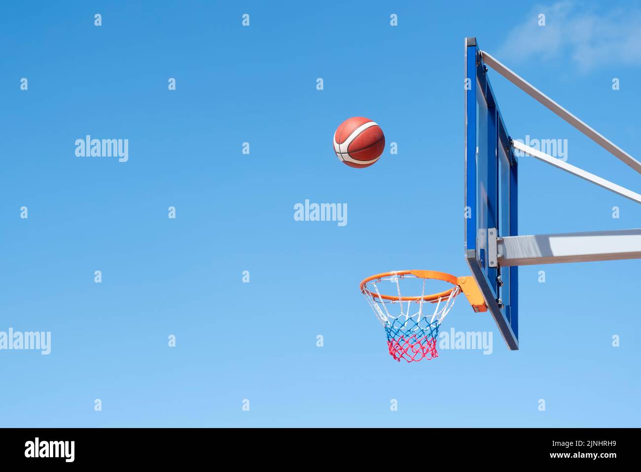 basketball in a net on a blue sky background. The ball hit the ring. Sports, team game. Conceptual: victory, success, hitting the target, sport. Stock Photo