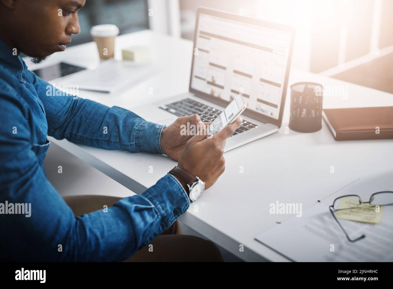 Using multiple devices to get the job done. Closeup shot of an unrecognizable businessman using a cellphone and laptop in an office. Stock Photo