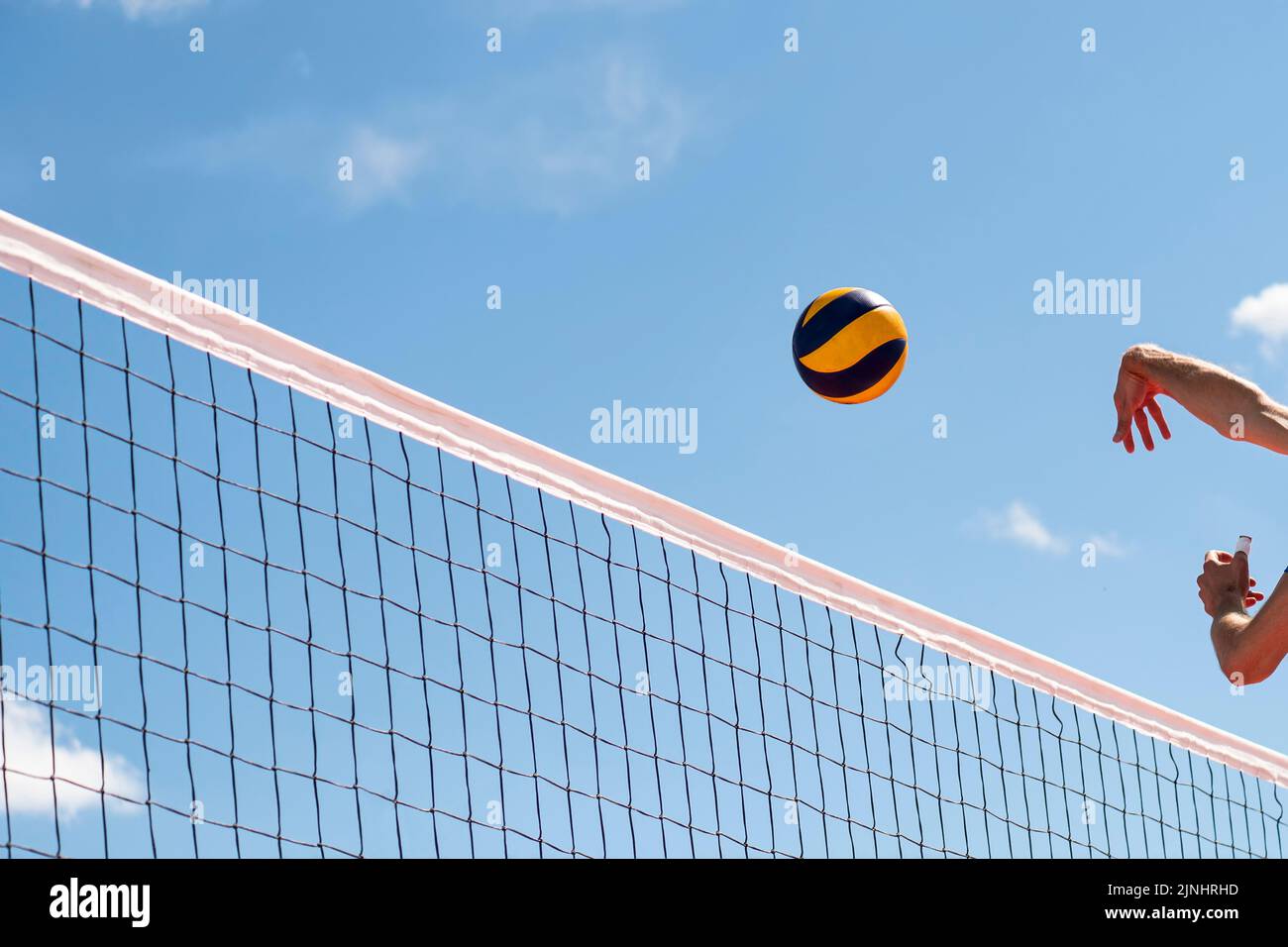Volleyball flying through air with hands visible against the background of a blue sky with clouds Stock Photo