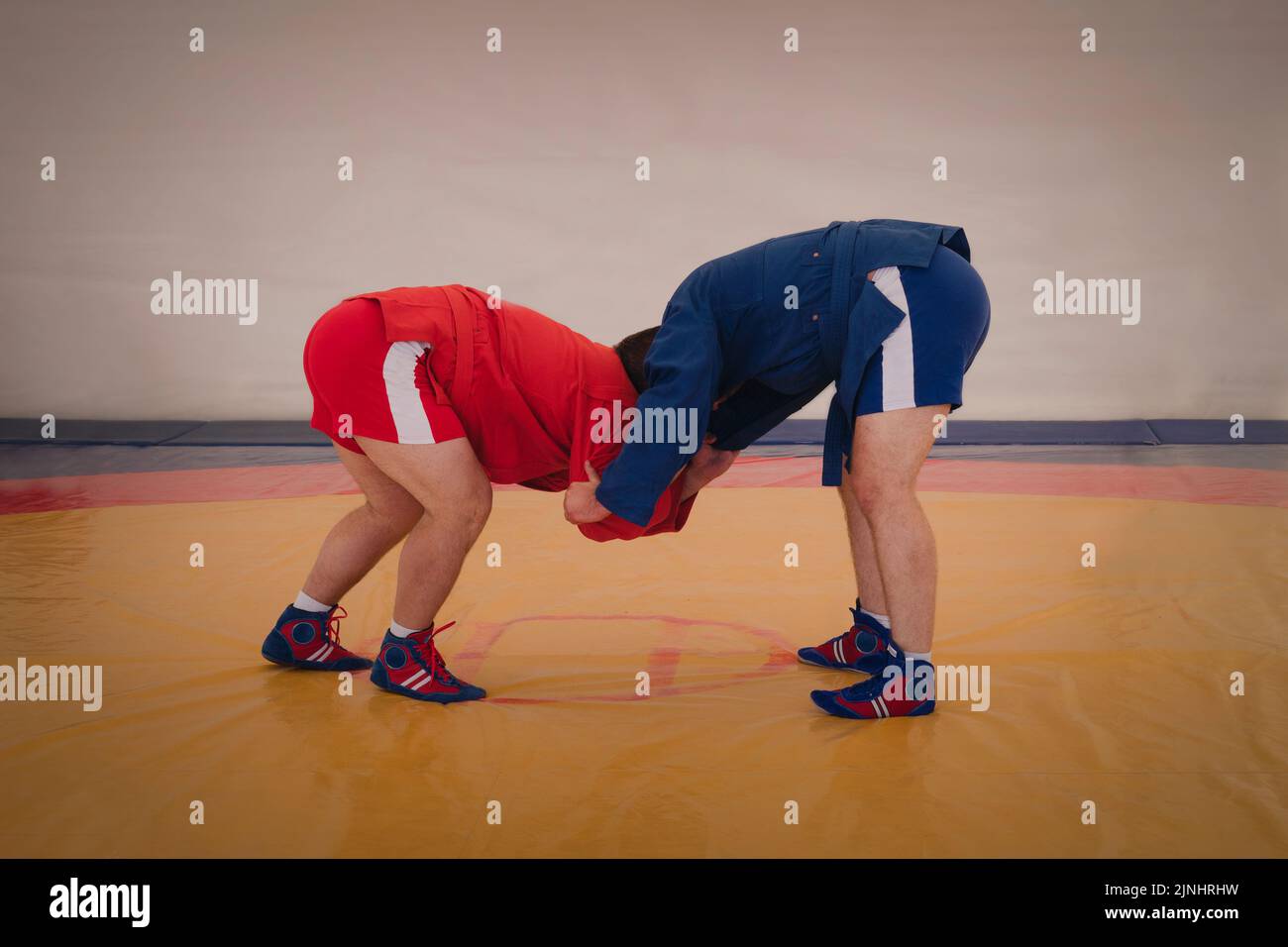two men in blue and red tights are wrestling on a yellow tatami. Sambo wrestlers train. Sambo competition in the hall. Stock Photo