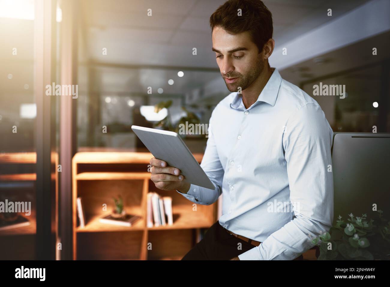 Knocking out deadline after deadline. a young businessman working late on a digital tablet in an office. Stock Photo