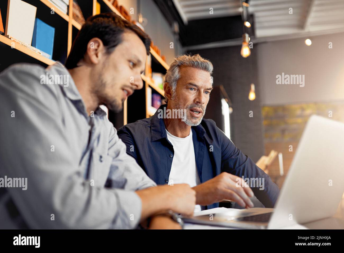 Putting in some extra work over the weekend. two handsome businessmen working together in a local internet cafe. Stock Photo