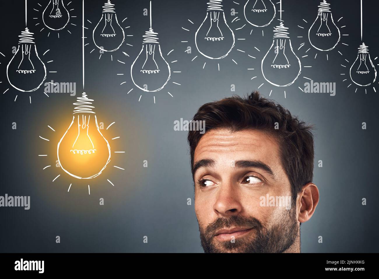 Hes onto something. Studio shot of a handsome young man standing beside an illustration of a lit light bulb against a grey background. Stock Photo