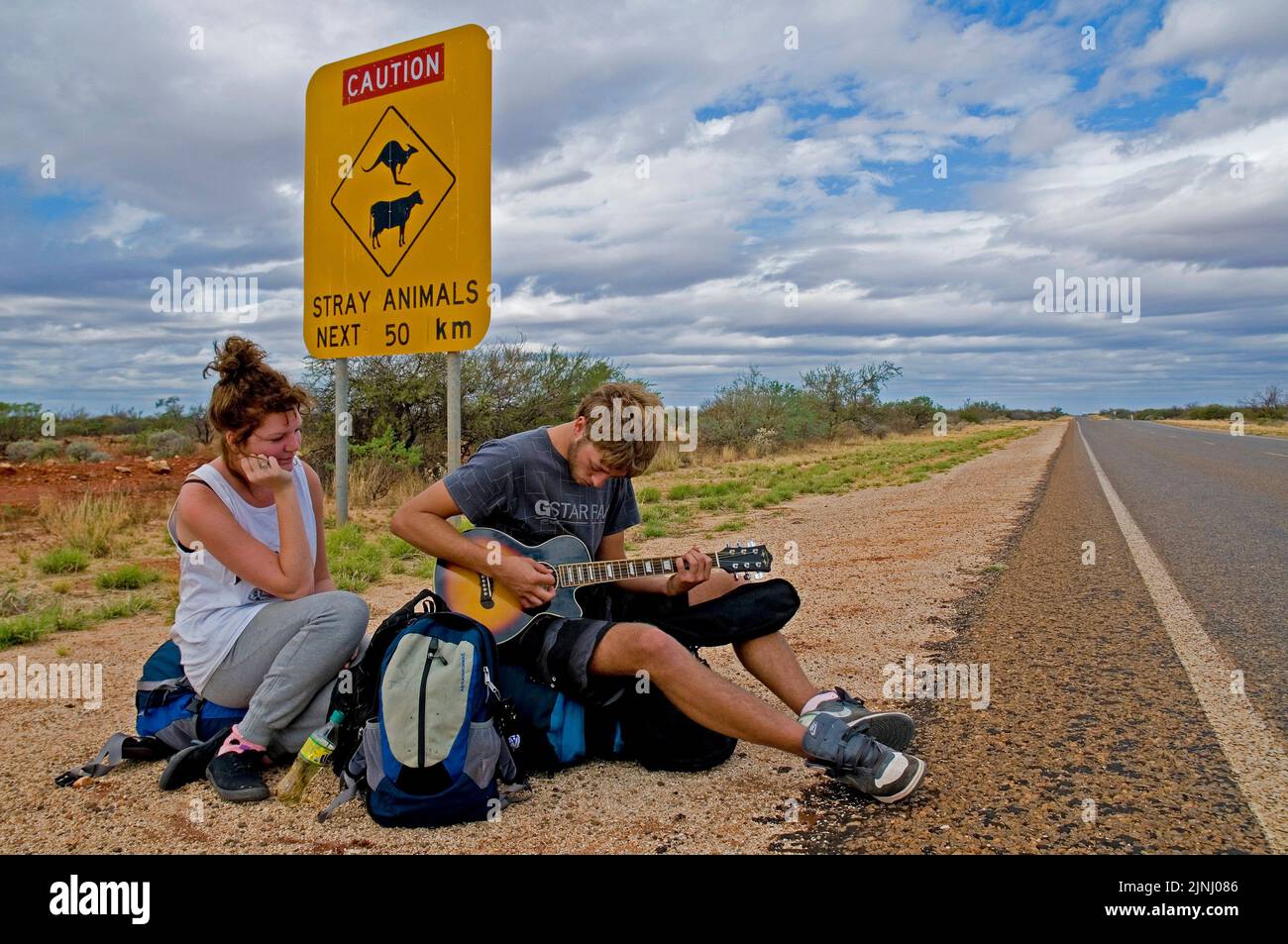 A couple of young British backpackers waiting for a lift on the highway near Monkey Mia in Western Australia Stock Photo