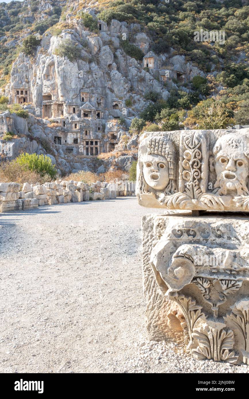 Vertical image of Historical Stone faces bas relief and ancient theater at Myra ancient city. Rock-cut tombs Ruins in Lycia region, Demre, Antalya. Stock Photo