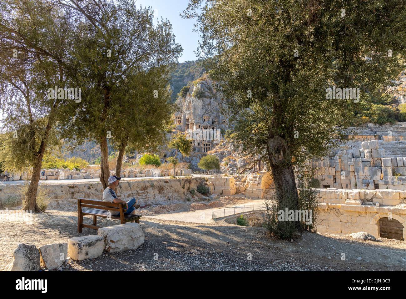 Historical Myra ancient city. The man is sitting in the shade under the trees on a sunny summer day. Rock-cut tombs Ruins in Lycia region. Stock Photo