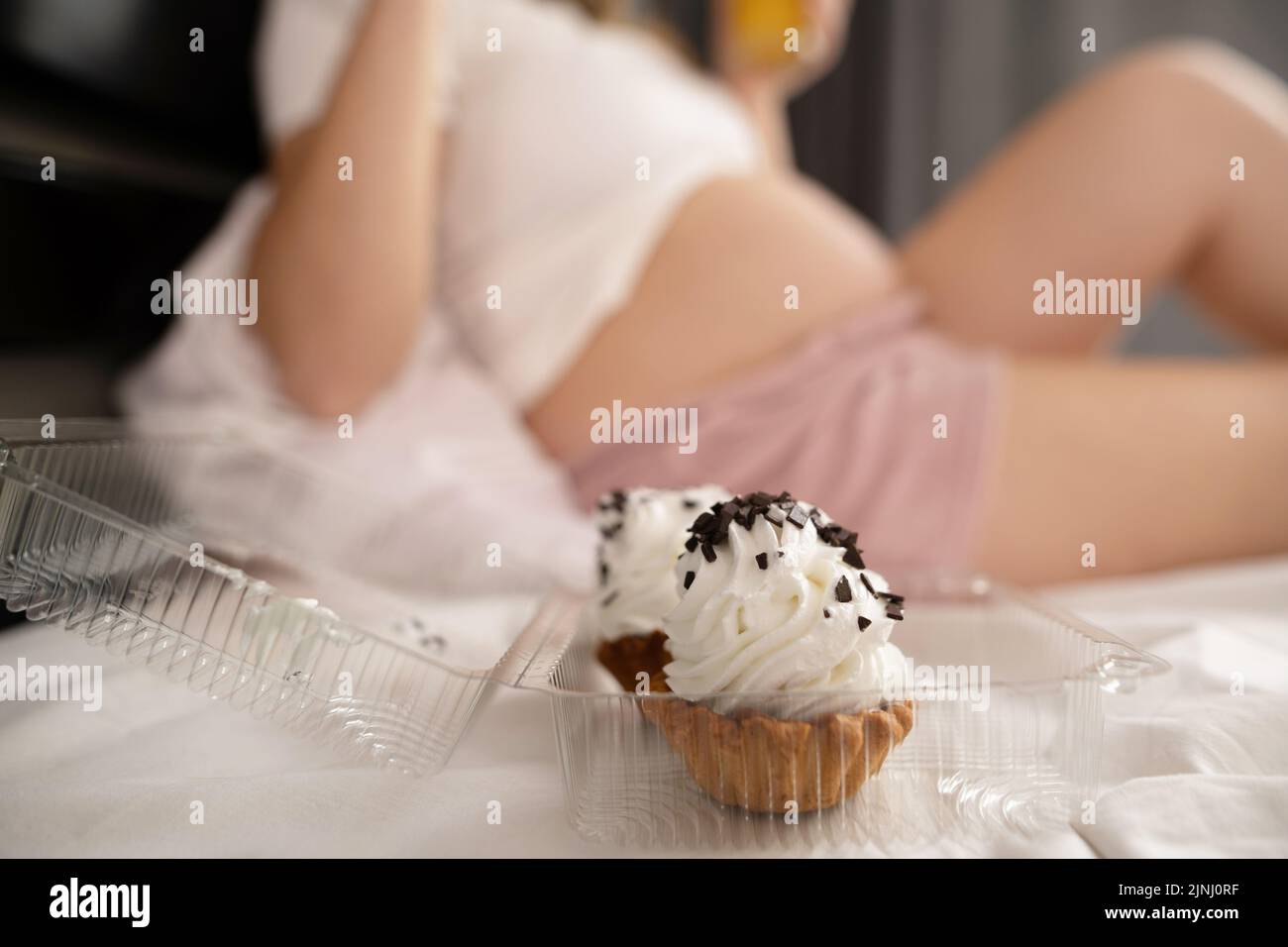 Close up of pregnant woman staying in bed to eat junk food, cakes. Healthy diet for future mother.Pregnancy and unhealthy eating concept Stock Photo