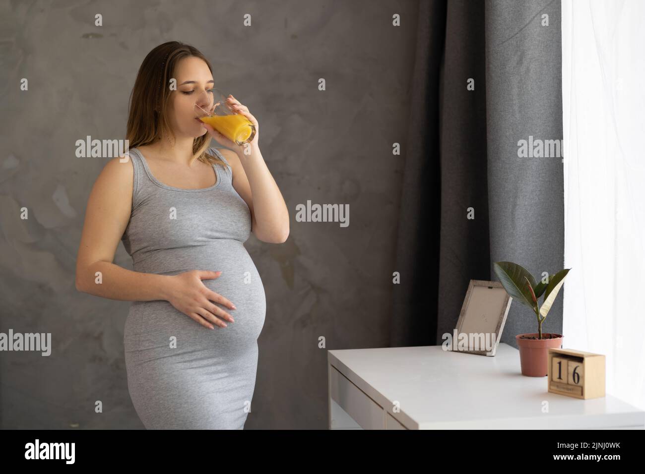 A pregnant woman drinking orange juice in the morning. Waiting for a