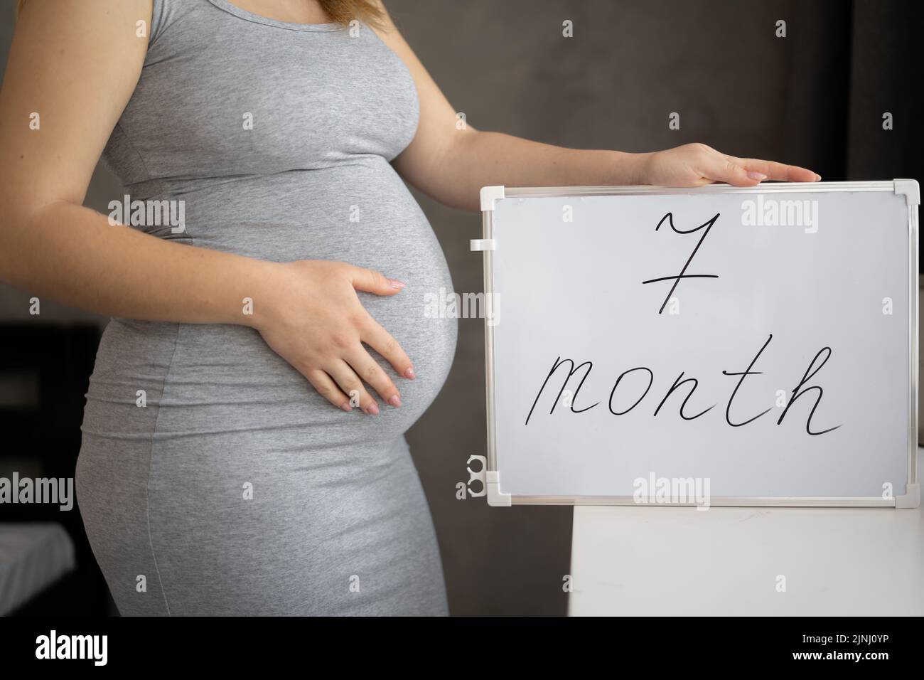 Close up of 7monthpregnant woman belly holding a whiteboard with text