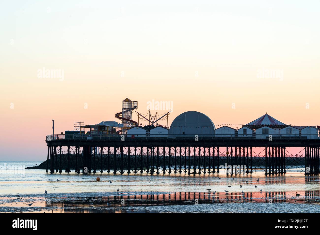 The beach and the pier at low tide during first light of the pastel-coloured dawn sky at the Kent resort town of Herne Bay. Stock Photo