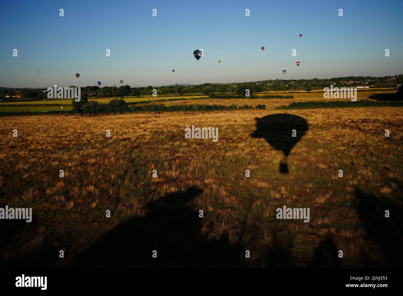 Balloons fly over a fields turned brown and dried out in the prolonged spell of dry weather during the Bristol International Balloon Fiesta 2022. Picture date: Friday August 12, 2022. Stock Photo
