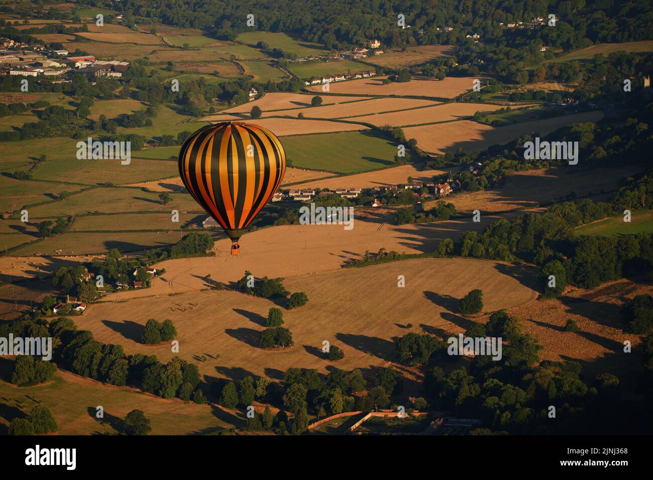 A balloon flies over fields which have turned brown and dried out in the prolonged spell of dry weather during the Bristol International Balloon Fiesta 2022. Picture date: Friday August 12, 2022. Stock Photo