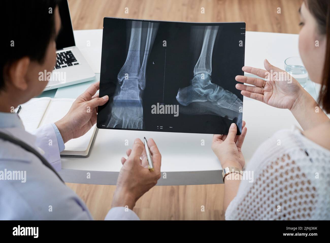 Over shoulder view of middle-aged surgeon showing foot X-ray to female patient while having appointment, close-up shot Stock Photo