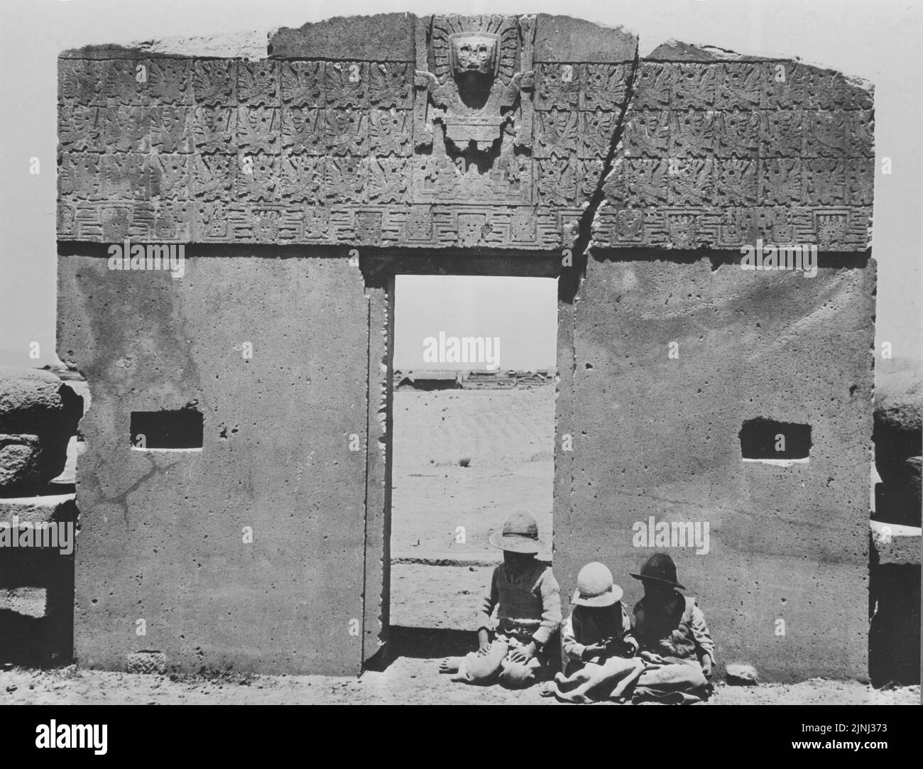 Early 20th century black and and white photograph showing children sitting in front of the Gate of the Sun or Puerta del Sol at the pre-Columbian ruins of Tiwanaku  near Lake Titicaca, Bolivia, South America 1920-147 LC Stock Photo