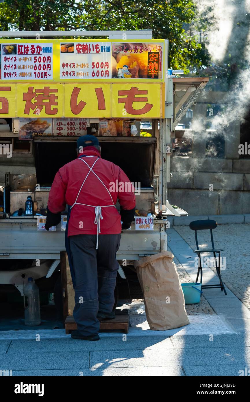 Chiyoda City, Tokyo, Japan - January 02, 2020: A Japanese man selling baked sweet potatoes outside the traditional Yasukuni Shinto Shrine. Stock Photo