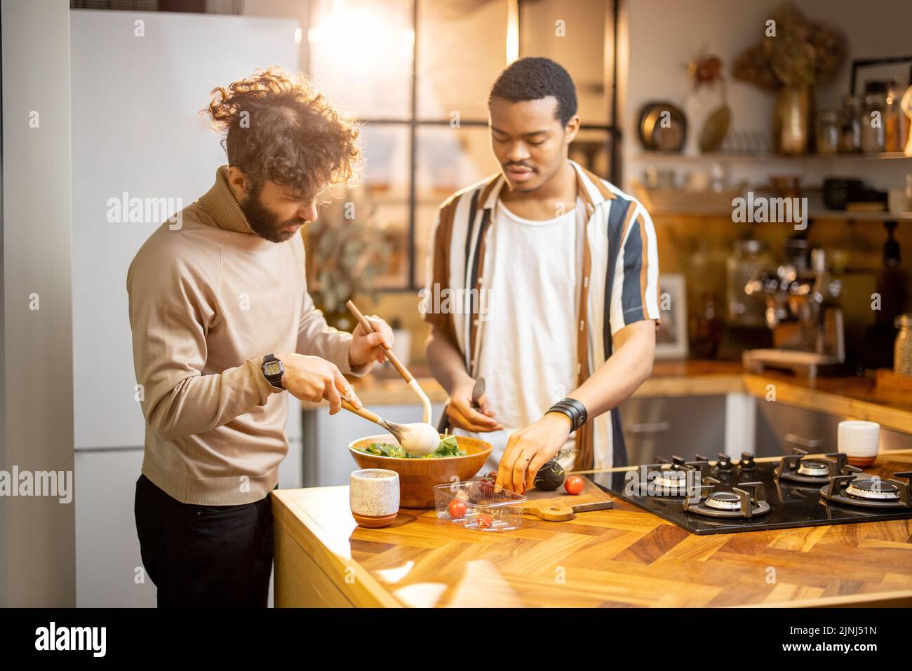Two guys of different ethnicity cooking healthy vegan food on kitchen at home. Concept of close male friendship or relationship as gay. Idea of health Stock Photo