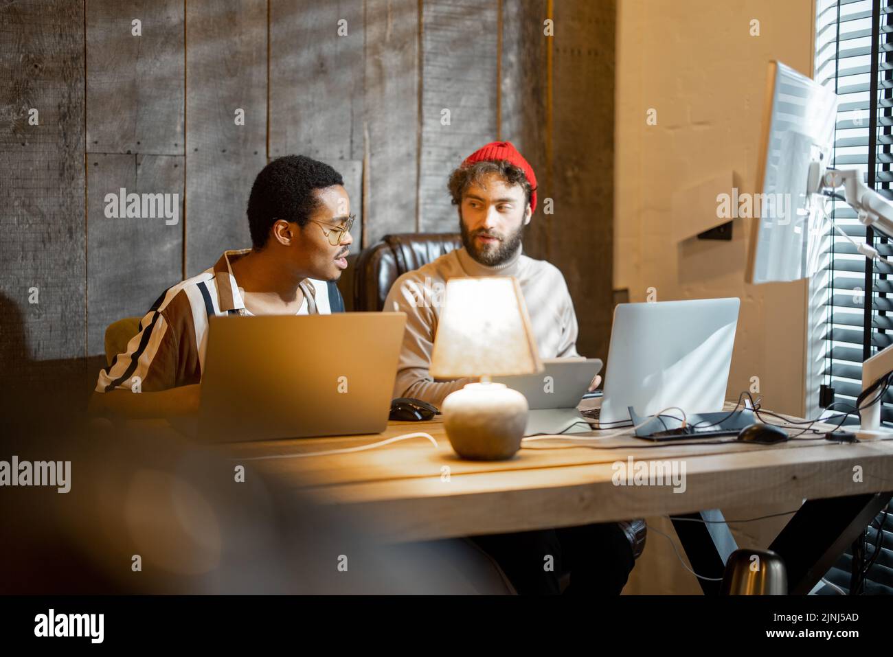 Two men with different nationality working on computers, sitting together at cozy home office. Concept of freelance and remote work. Stylish male hips Stock Photo