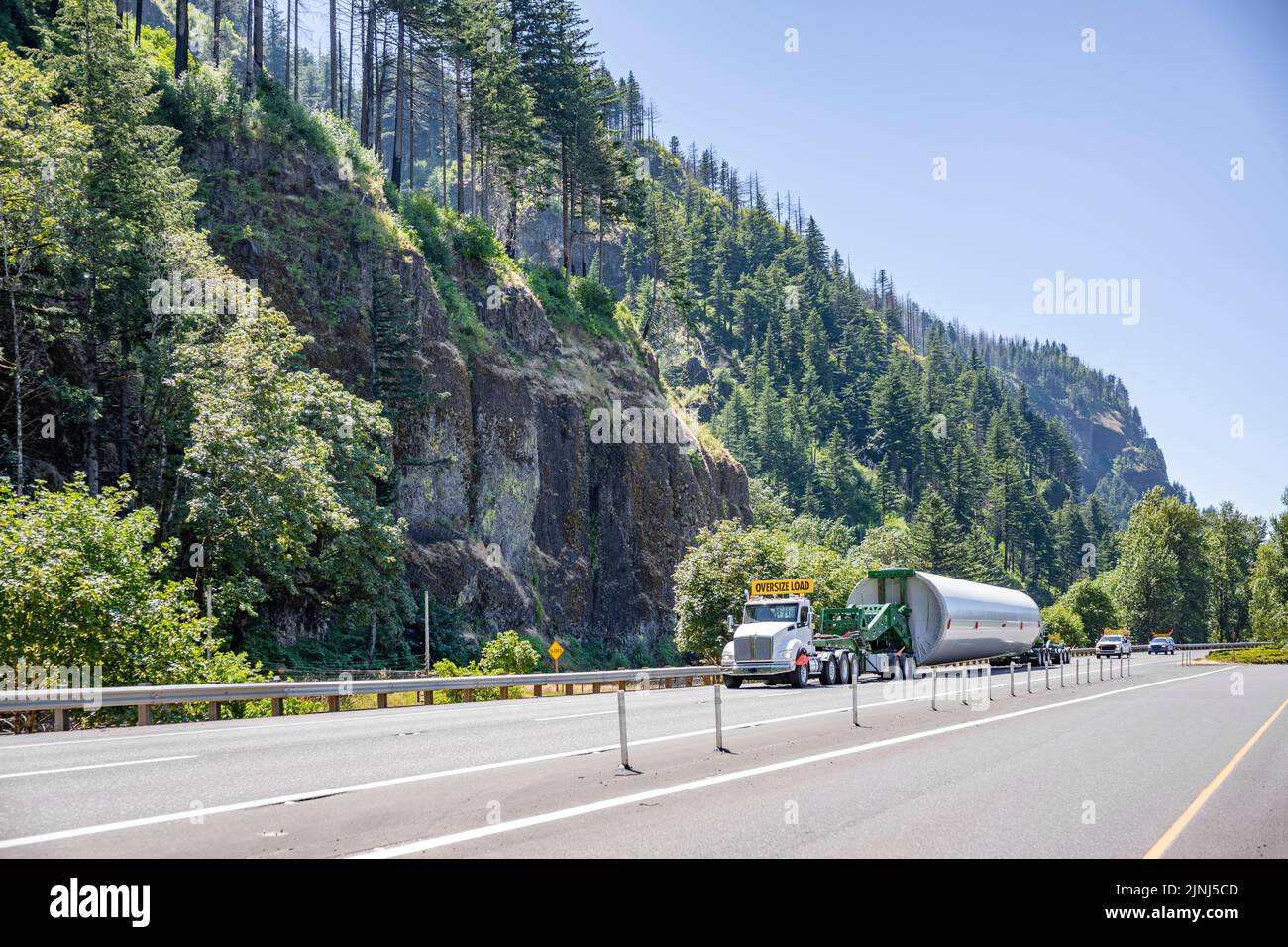 Heavy duty big rig semi truck transporting part of long oversized windmill electric generator pole on the specialized semi trailer with additional tro Stock Photo