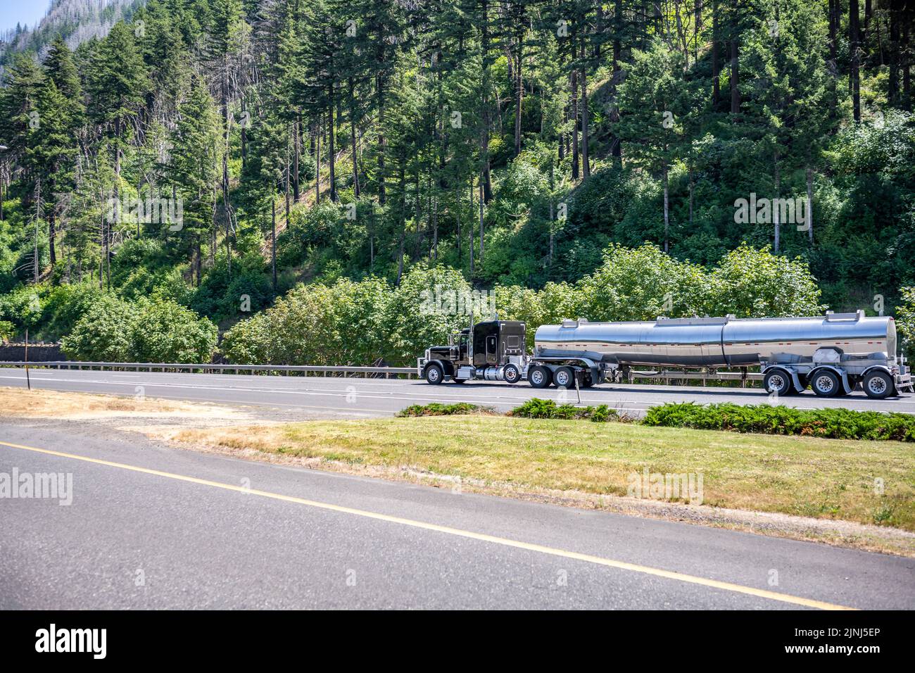 Industrial standard black classic shiny powerful big  rig semi truck tractor transporting liquid cargo in stainless steel tank semi trailer running on Stock Photo
