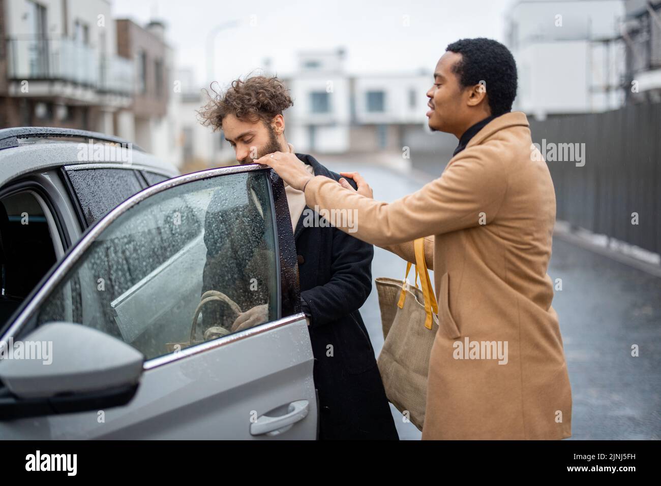 Two men flirting or having a close conversation while opening car door on the street. Concept of homosexual relations or close male friendship. Caucas Stock Photo