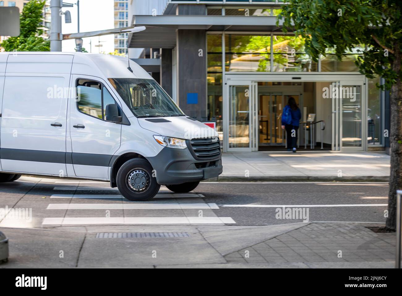 Industrial standard for local deliveries and short haul freights or small business services compact white mini van turning to building parking garage Stock Photo