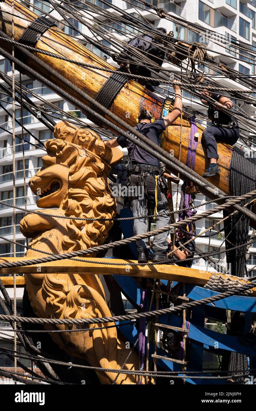 Crew members of the replica sailing ship, Gotheborg, perform repairs and maintenance at the ship's figurehead while docked beneath the high-rise towers at South Quay, Canary Wharf in London Docklands, during its four-day visit to the capital before it continues its two-year around the world expedition to Shanghai, China, on 9th August 2022, in London, England. Londoners are invited to tour the decks of this facsimile of the original ship which sank off the Swedish coast in 1745. Its main cargo would have been tea, porcelain, herbs and silk on the China route. (Photo by Richard Baker / In Pictu Stock Photo
