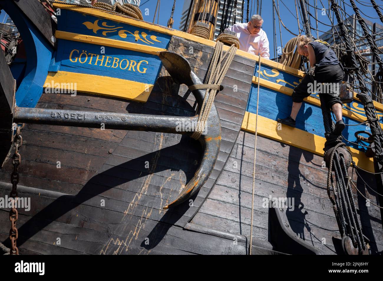 The crew of the replica sailing ship, Gotheborg, perform repairs and maintenance while docked beneath the high-rise towers at South Quay, Canary Wharf in London Docklands, during its four-day visit to the capital before it continues its two-year around the world expedition to Shanghai, China, on 9th August 2022, in London, England. Londoners are invited to tour the decks of this facsimile of the original ship which sank off the Swedish coast in 1745. Its main cargo would have been tea, porcelain, herbs and silk on the China route. Stock Photo