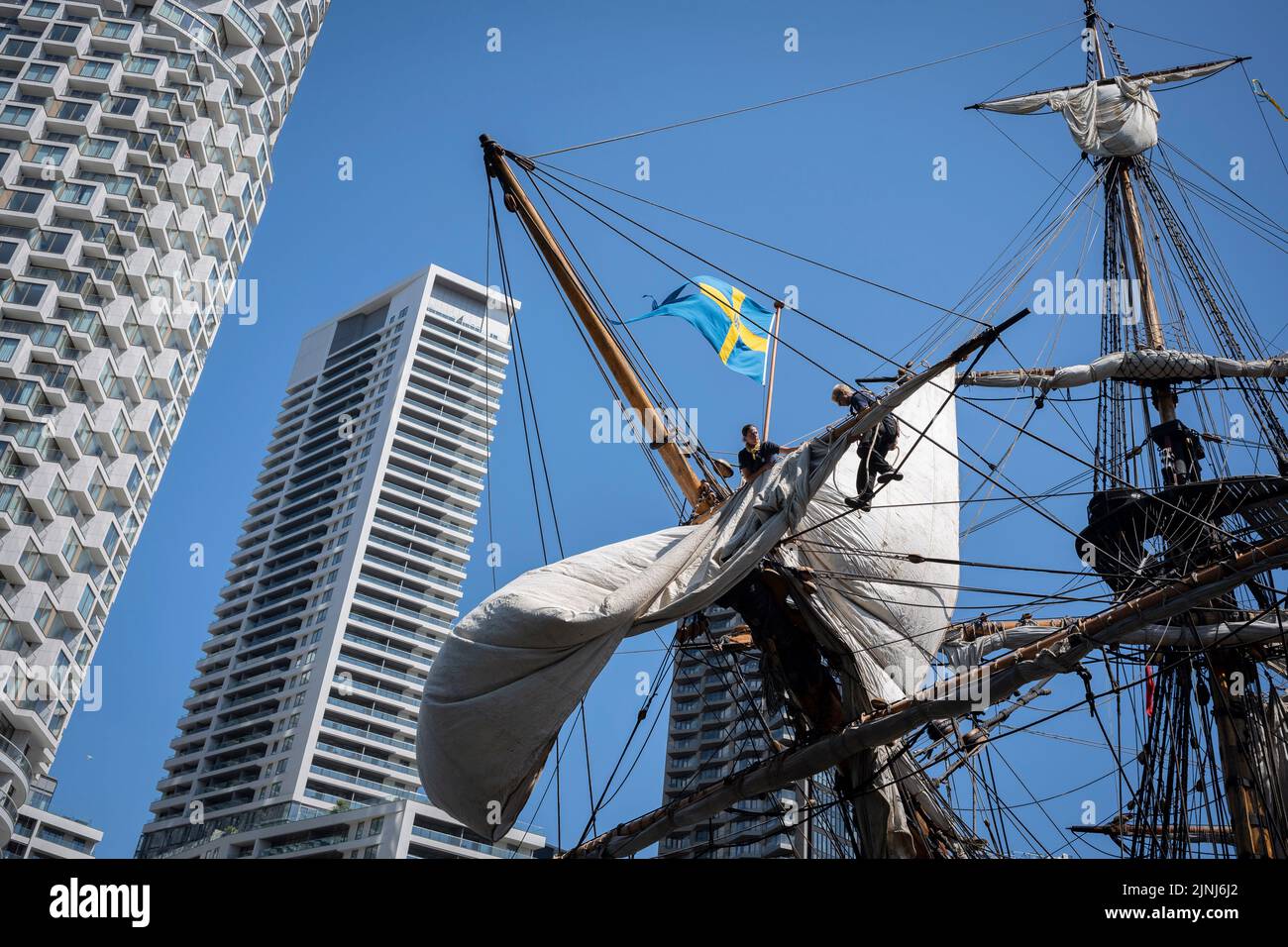 The crew of the replica sailing ship, Gotheborg, perform repairs and maintenance while docked beneath the high-rise towers at South Quay, Canary Wharf in London Docklands, during its four-day visit to the capital before it continues its two-year around the world expedition to Shanghai, China, on 9th August 2022, in London, England. Londoners are invited to tour the decks of this facsimile of the original ship which sank off the Swedish coast in 1745. Its main cargo would have been tea, porcelain, herbs and silk on the China route. Stock Photo