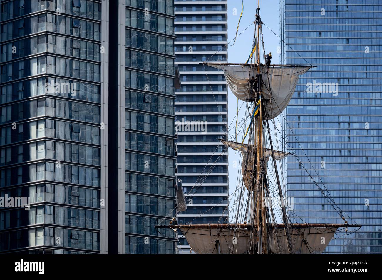 The crew of the replica sailing ship, Gotheborg, perform repairs and maintenance up the tall rigging while docked beneath the high-rise towers at South Quay, Canary Wharf in London Docklands, during its four-day visit to the capital before it continues its two-year around the world expedition to Shanghai, China, on 9th August 2022, in London, England. Londoners are invited to tour the decks of this facsimile of the original ship which sank off the Swedish coast in 1745. Its main cargo would have been tea, porcelain, herbs and silk on the China route. Stock Photo