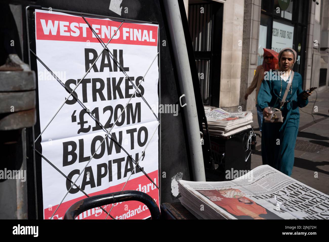 Days before the next RMT national rail strike takes effect at the weekend, the public walk past the latest Evening Standard newspaper headline during the August heatwave in the City of London, the capital's financial district, on 11th August 2022, in London, England. Stock Photo