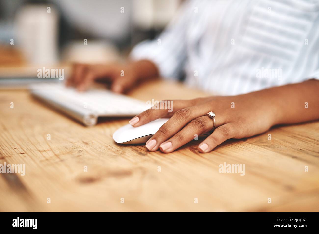 Hand on a mouse, clicking and scrolling while browsing online and surfing the internet. Closeup of a woman using a computer while sitting at a wooden Stock Photo