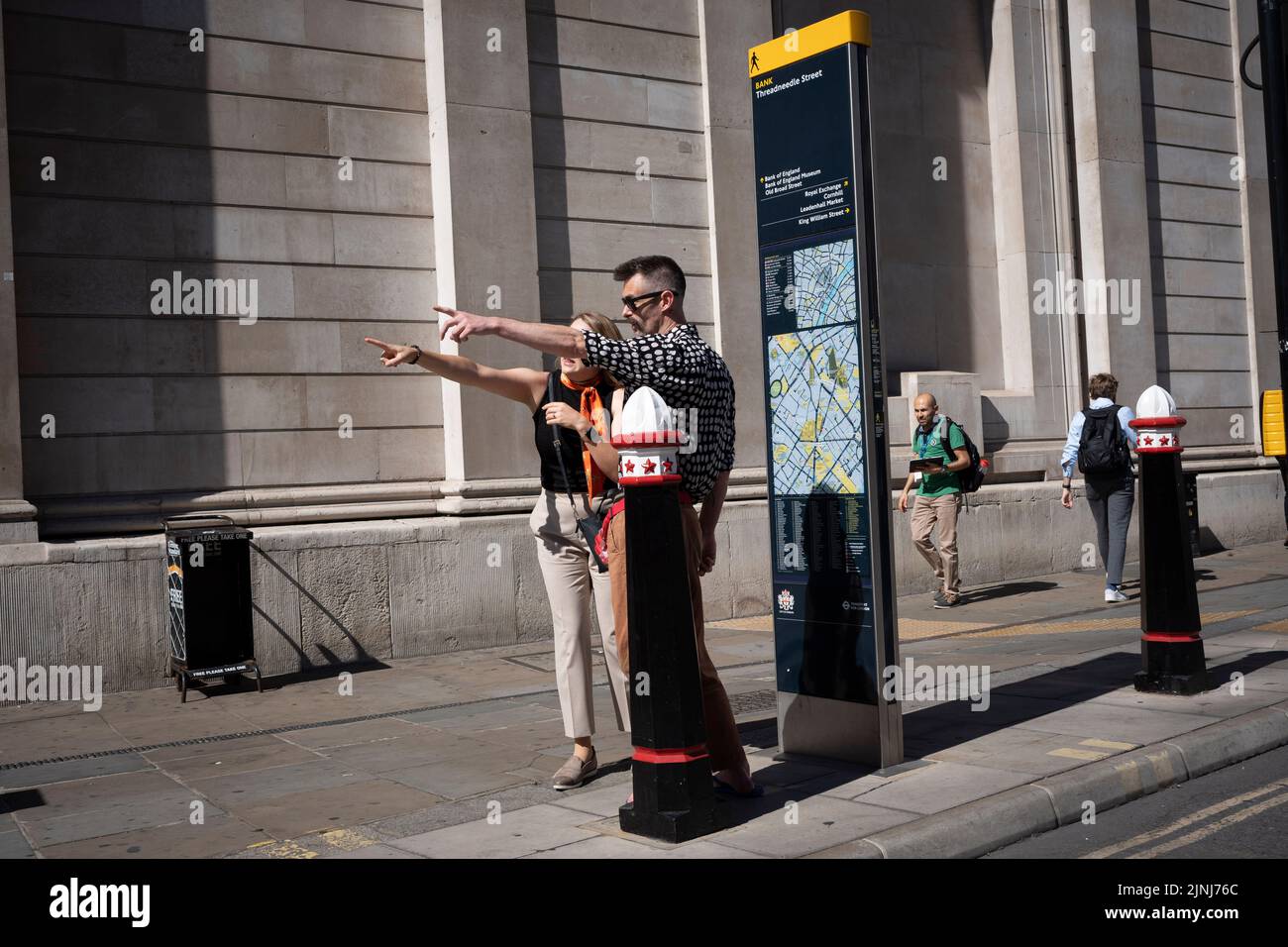 A stranger stops beneath the walls of the Bank of England to help a visitor to the capital with diirections in the City of London, the capital's financial district (aka the Square Mille), on 10th August 2022, in London, England. Stock Photo