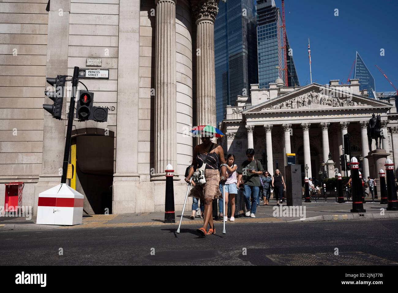 During the August heatwave, a woman wearing a head shade, crosses the road outside the Bank of England in the City of London, the capital's financial district (aka the Square Mille), on 10th August 2022, in London, England. Stock Photo