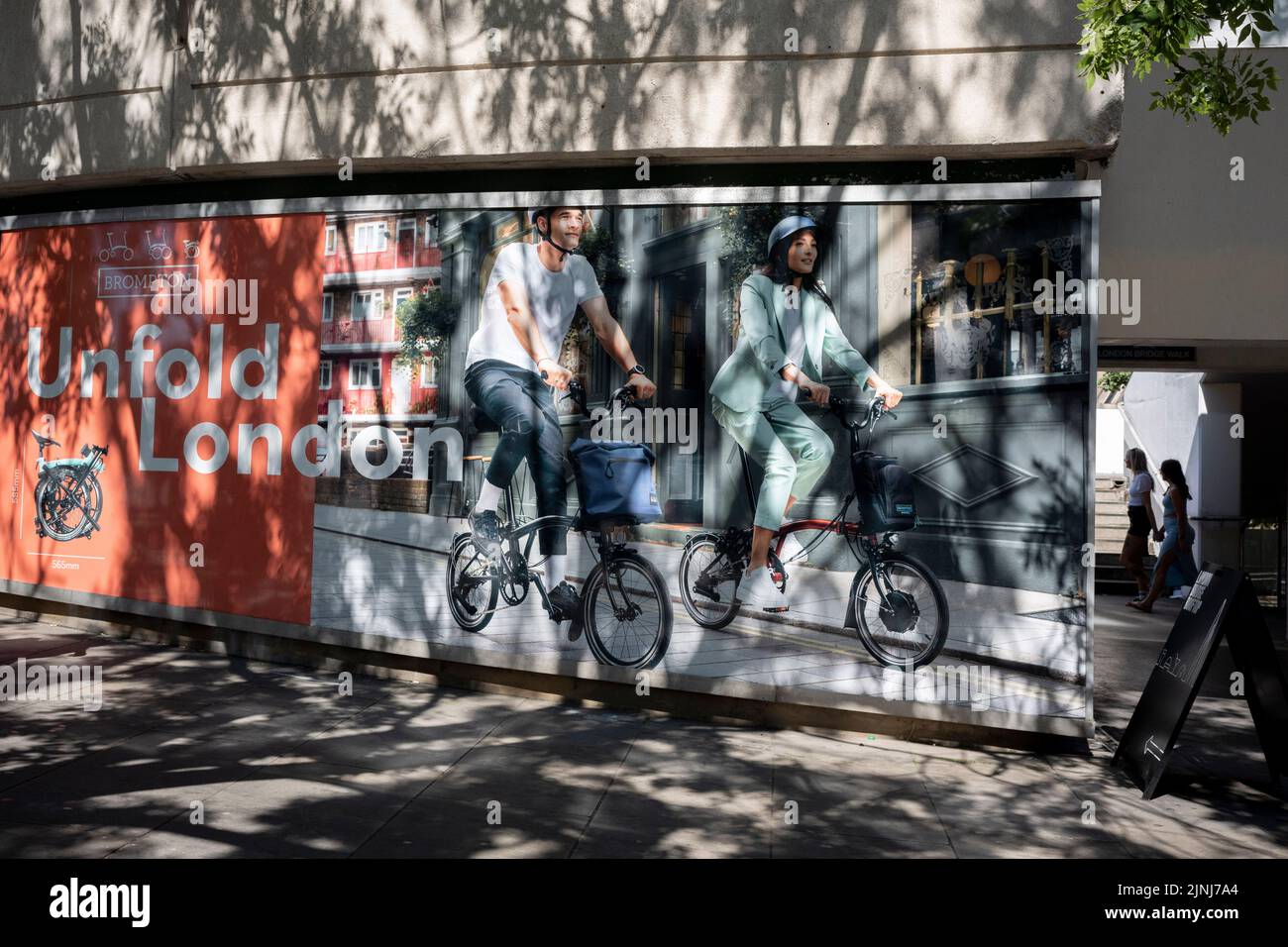 Londoners walk past a billboard ad for the folding bike brand, Brompton