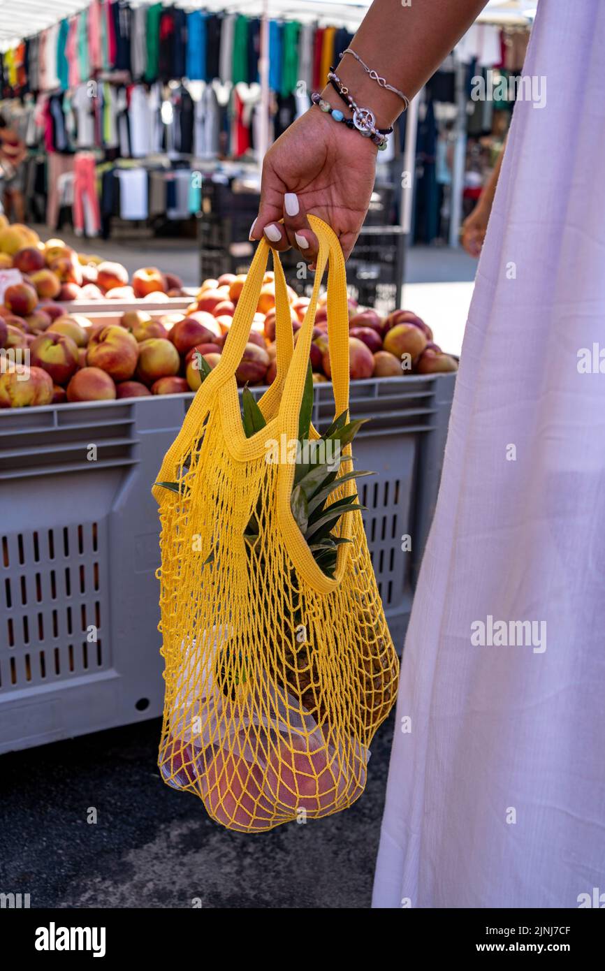Woman in white dress with shopping in reusable cotton net bag at local market, zero waste concept. Stock Photo